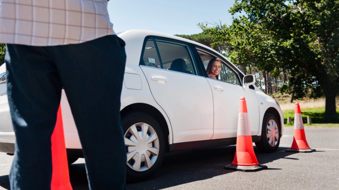 Une candidate au permis de conduire effectue un exercice pratique sous la supervision d’un examinateur, entourée de cônes de signalisation.